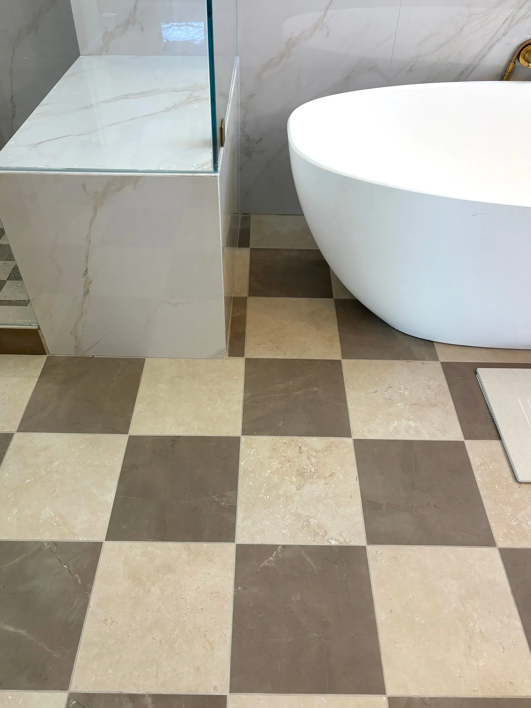 Marble-clad screen and glass panel beside the tub, with the checkerboard stone floor below