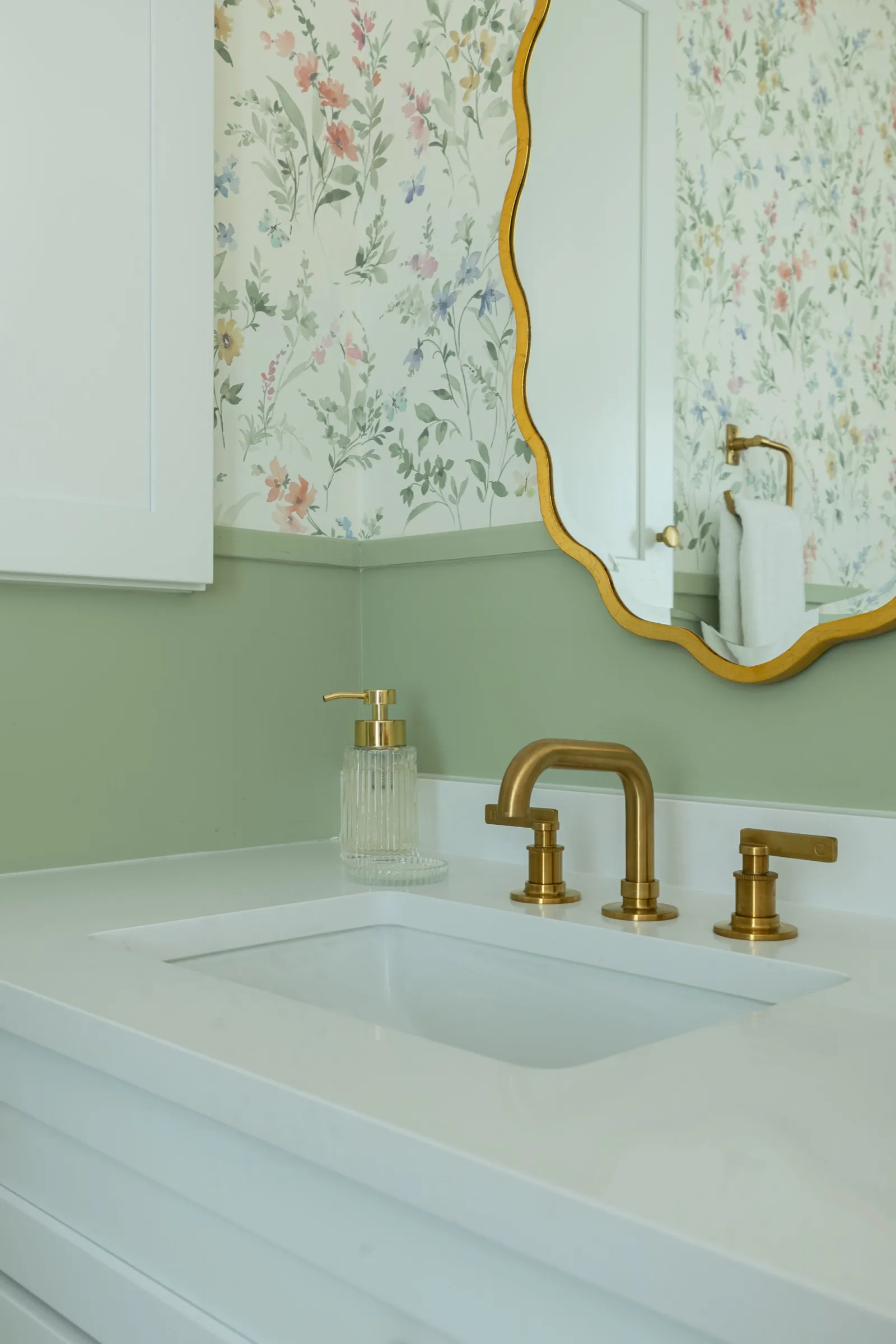 Brass tap on the white stone counter with the wavy gilded mirror reflecting the wildflower paper