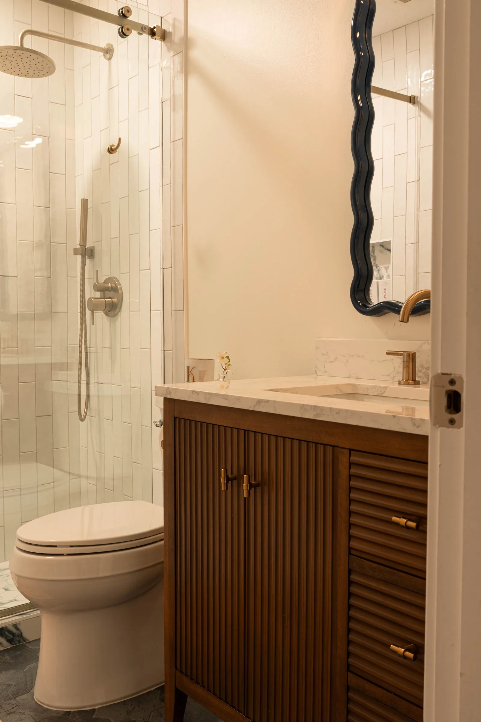 Fluted walnut vanity with a marble top, brass tap and a navy wave-edged mirror