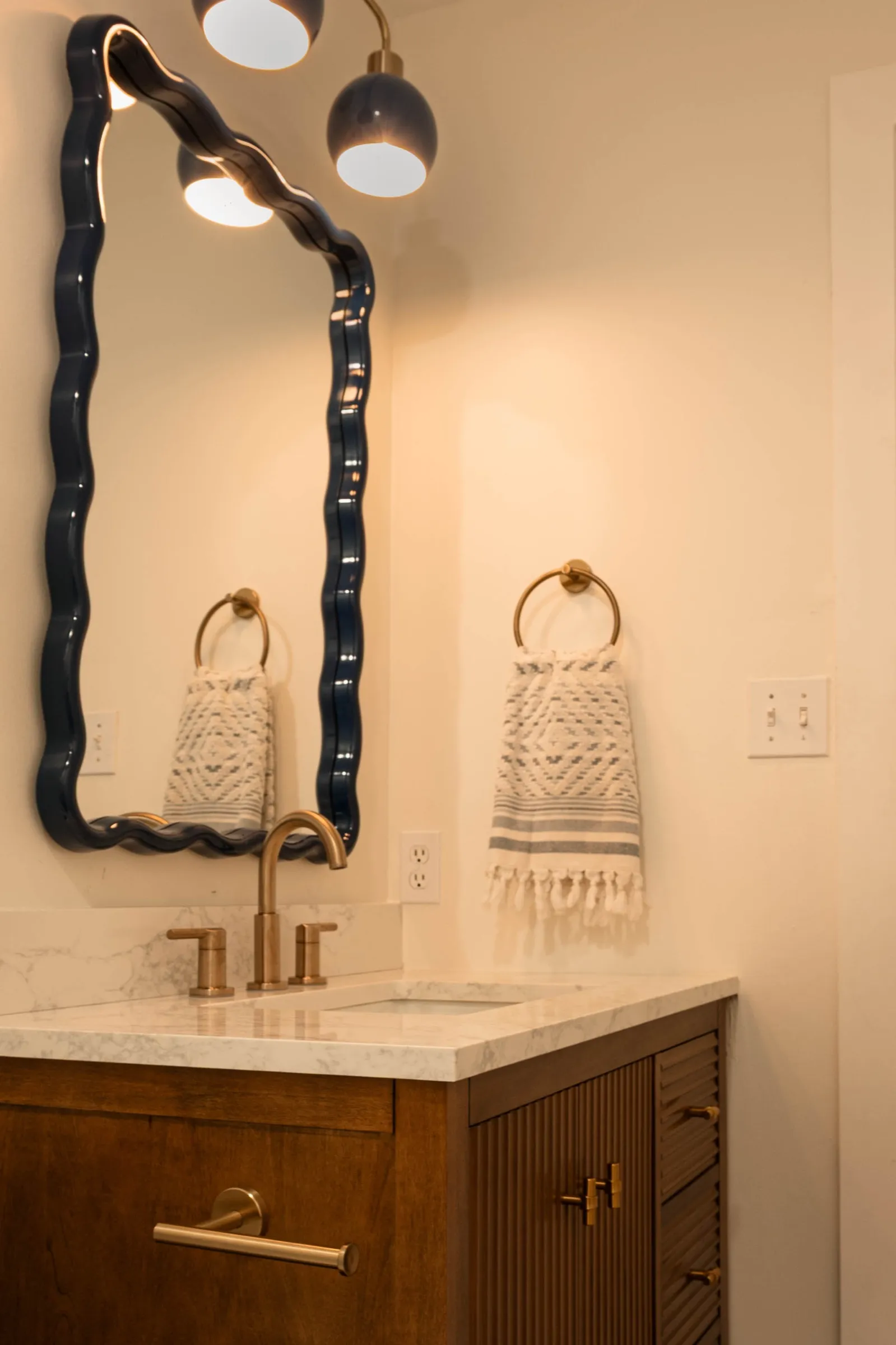 The navy wave-edged mirror above the walnut vanity, with a woven towel ring alongside