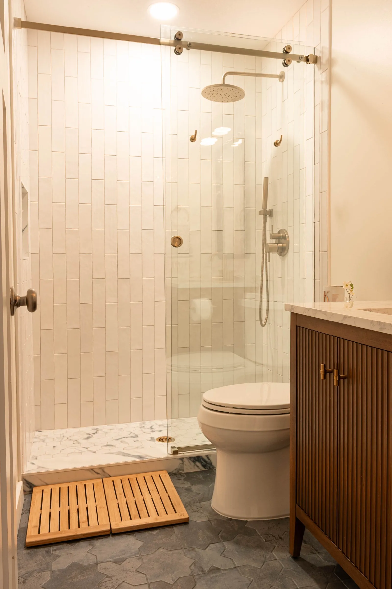 Shower lined in stacked white tile with brass fittings and a glass screen