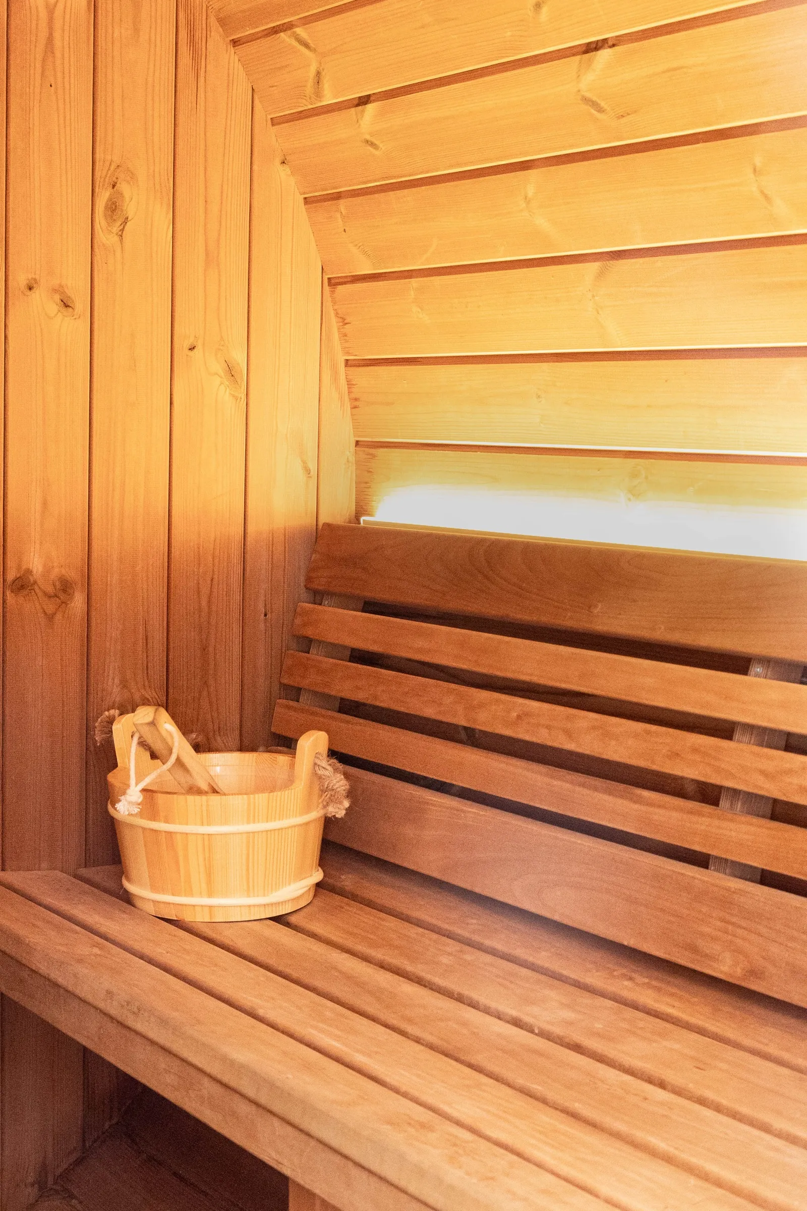 Inside the cedar barrel sauna, slatted benches and a wooden bucket and ladle