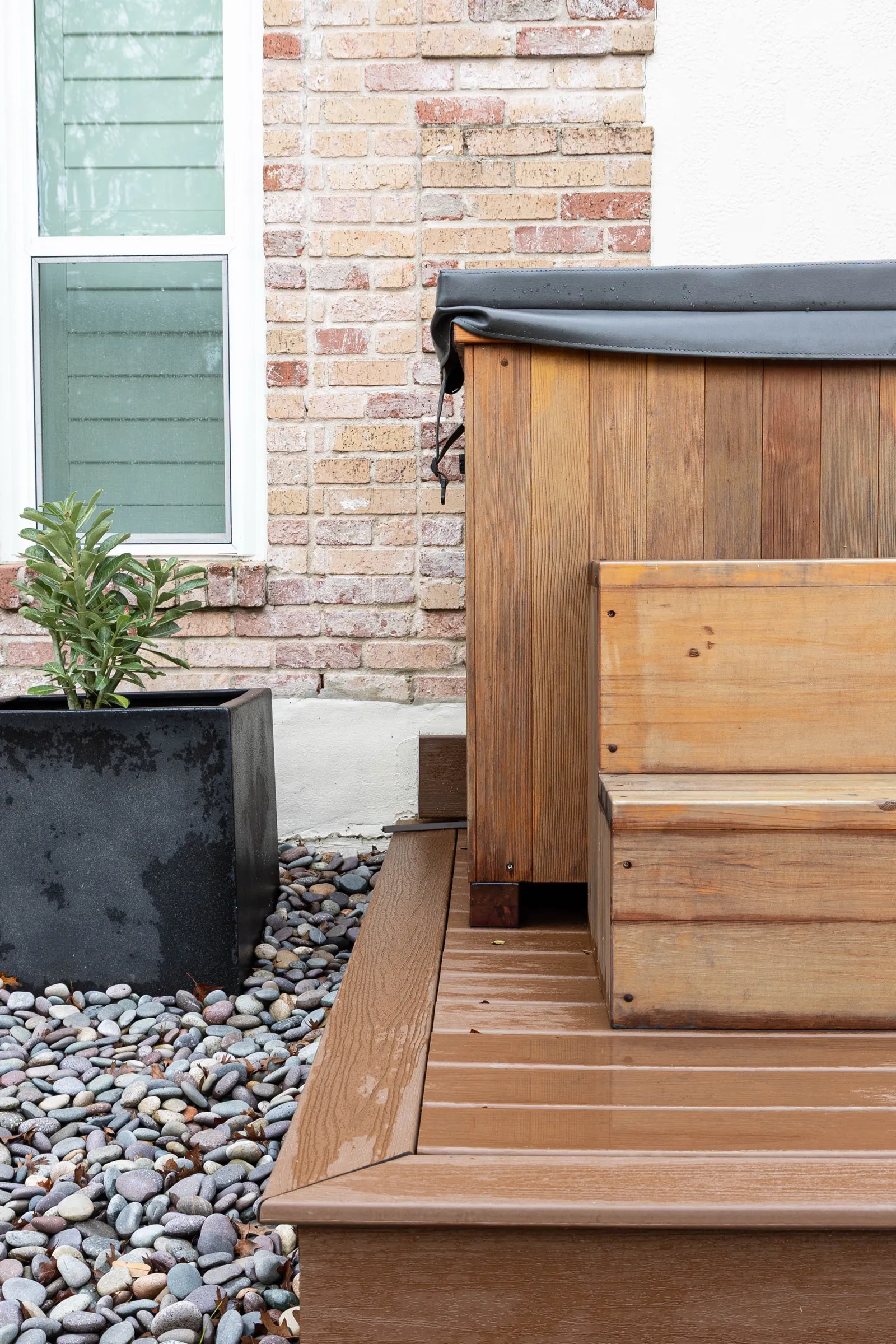 Cedar cold plunge tub under its insulated cover, set on the deck against the brick wall