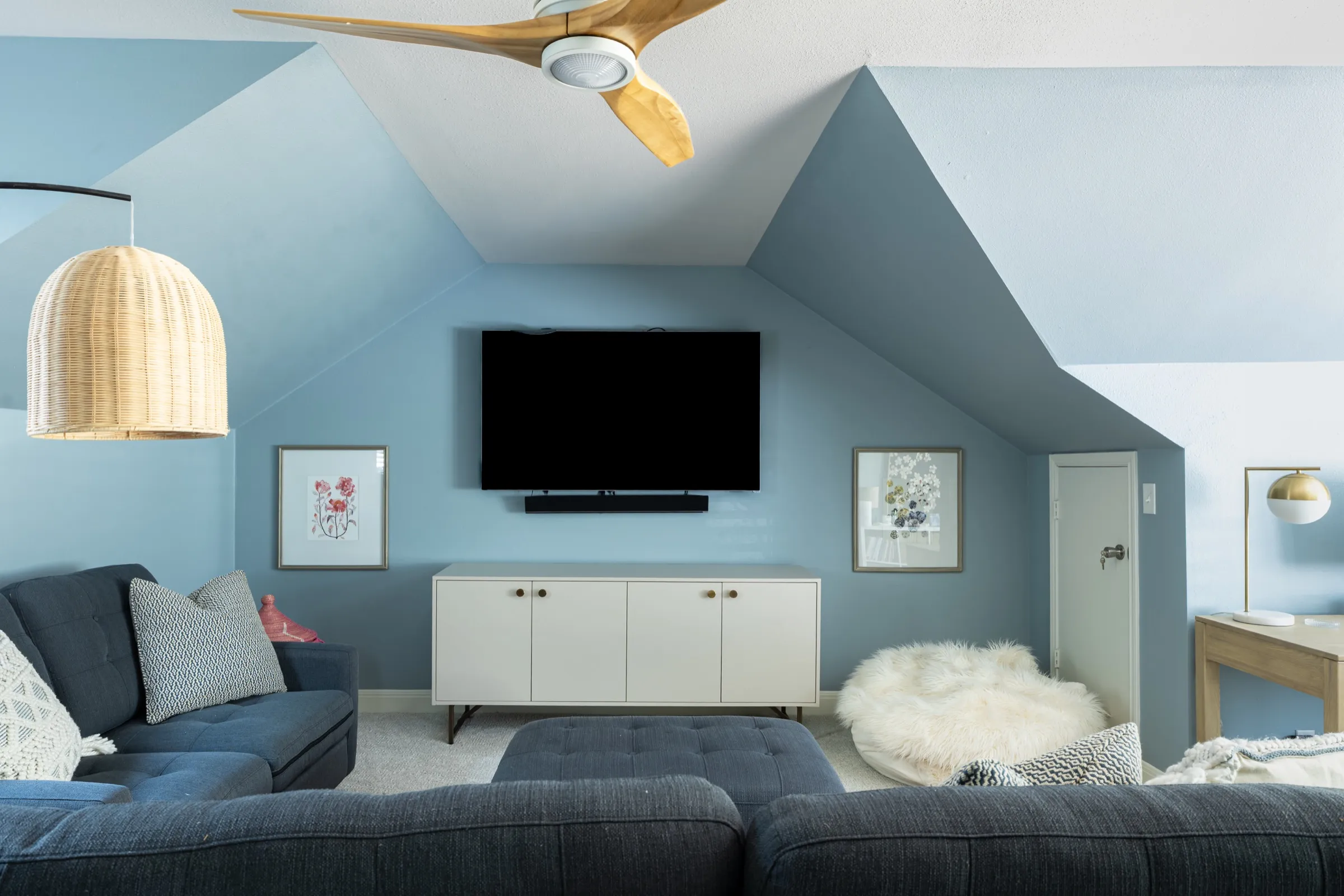 Blue family room under a sloping ceiling with a navy sectional, a woven pendant and a sheepskin floor cushion